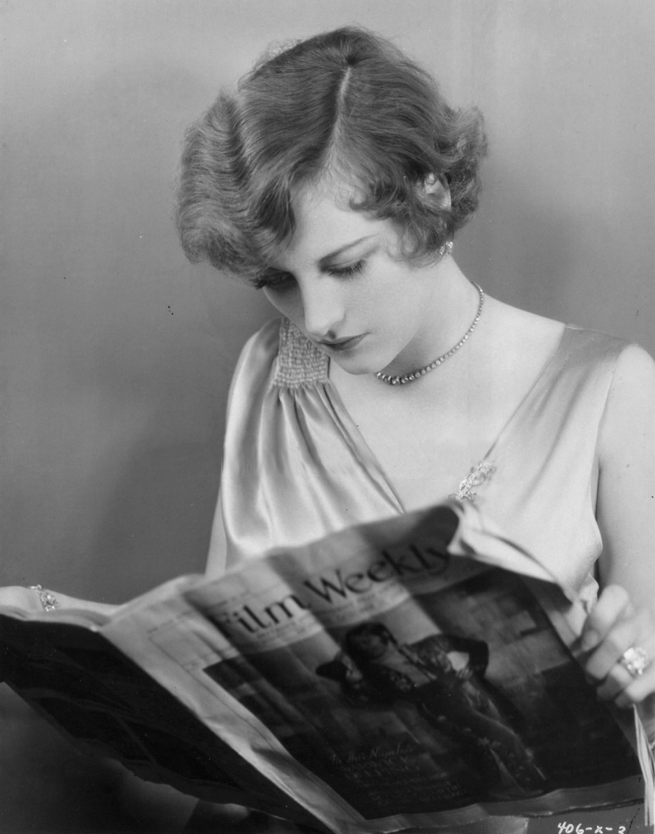 1929. On the set of 'The Duke Steps Out.' Reading a 'Film Weekly' with herself on the cover.
