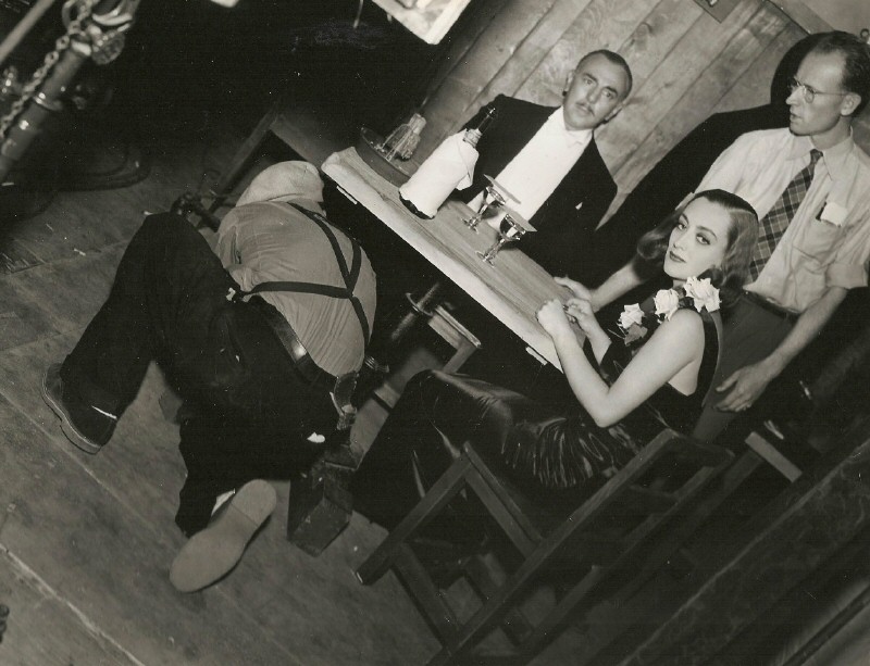 1937. On the set of 'The Bride Wore Red.' Prop man Harry Edwards under the table.