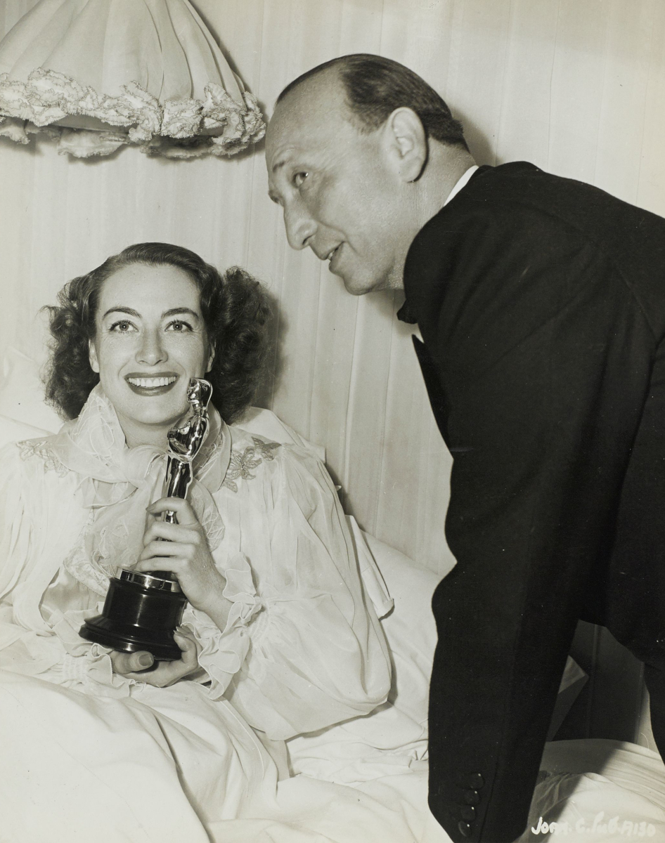 3/7/46. Joan receives her 'Mildred Pierce' Oscar in bed from director Michael Curtiz.