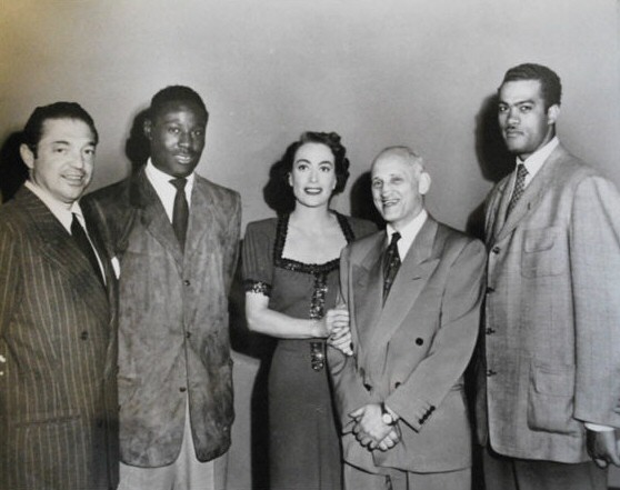 1950. On the set of 'Damned Don't Cry.' Director Vince Sherman on left, others unknown.