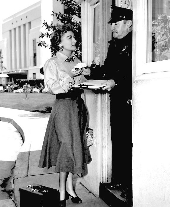 1953. On the MGM set of 'Torch Song' with gardenia and guard.