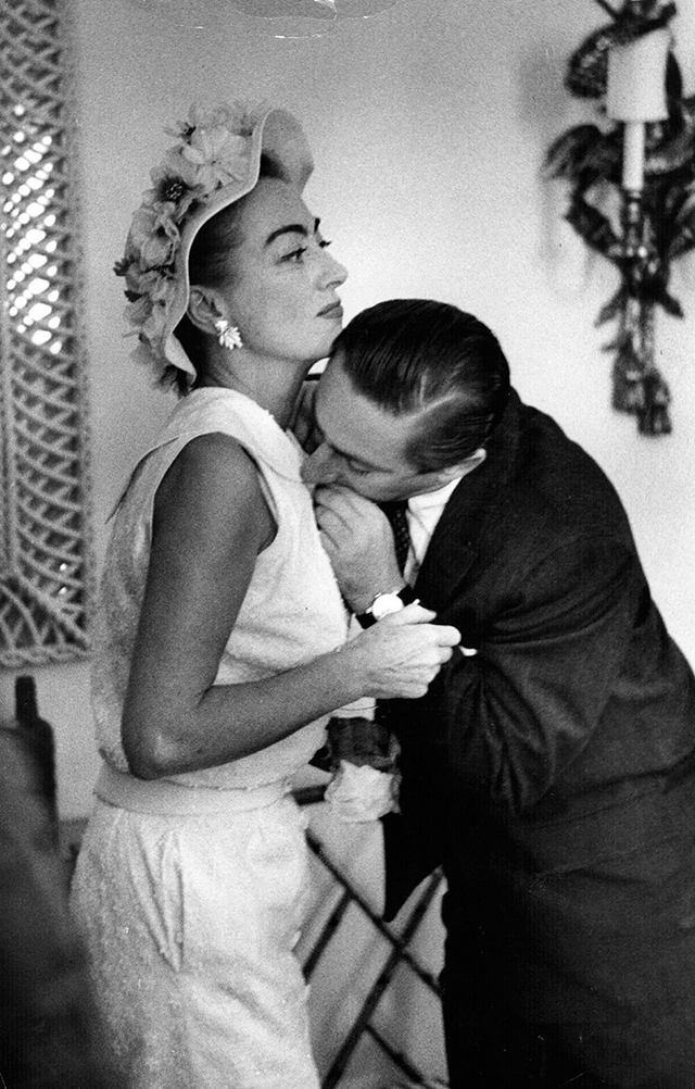 July 1956 at the Dorchester Hotel. An assistant bites a loose thread off Joan's dress. Photo by Thurston Hopkins.