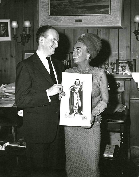 1964. Cartoonist Milton Caniff presents Joan with a 'Dragon Lady' birthday greeting.