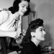 1942. On the set of 'They All Kissed the Bride' with hairdresser. Includes press caption.